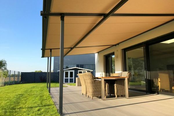 Eine Terrasse mit Korbmöbeln liegt wunderschön unter einer gut angebrachten Markise, neben einem Haus mit Schiebetüren. Sie bietet einen ruhigen Blick auf den Rasen und einen malerischen Schuppen.