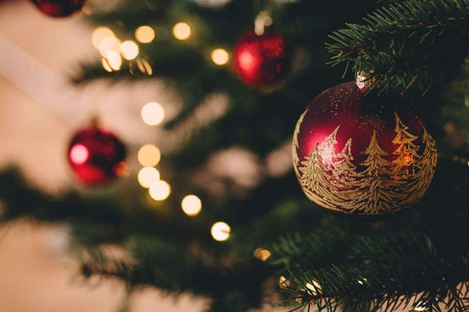 Nahaufnahme eines geschmückten Weihnachtsbaums mit roten Ornamenten und warmen Lichterketten, die ein gemütliches Licht verbreiten, das an die Atmosphäre unter einer stilvollen Markise erinnert.