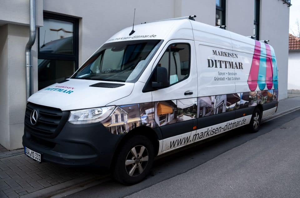 Auf der Straße parkt ein weißer Lieferwagen mit dem Schriftzug „Markisen Dittmar“, der auf die Kompetenz des Fachbetriebs für Markisenmontage hinweist.