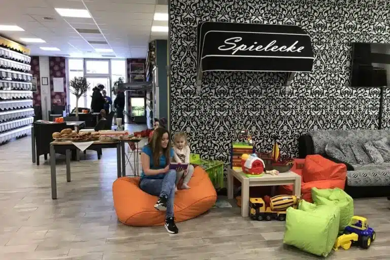 Eine Frau und ein Kind genießen es, in einer gemütlichen Spielecke, umgeben von Spielzeug und gemusterten Wänden, auf Sitzsäcken zu lesen, während die vom Fachbetrieb installierte Beschattung zur intimen Atmosphäre beiträgt.