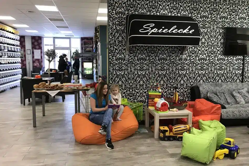 Eine Frau und ein Kind genießen es, in einer gemütlichen Spielecke, umgeben von Spielzeug und gemusterten Wänden, auf Sitzsäcken zu lesen, während die vom Fachbetrieb installierte Beschattung zur intimen Atmosphäre beiträgt.