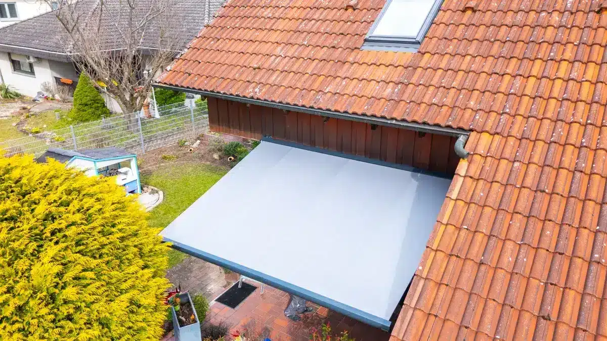 Luftaufnahme eines Hauses mit einem roten Ziegeldach und einer ausgefahrenen grauen Markise über einer kleinen Terrasse.