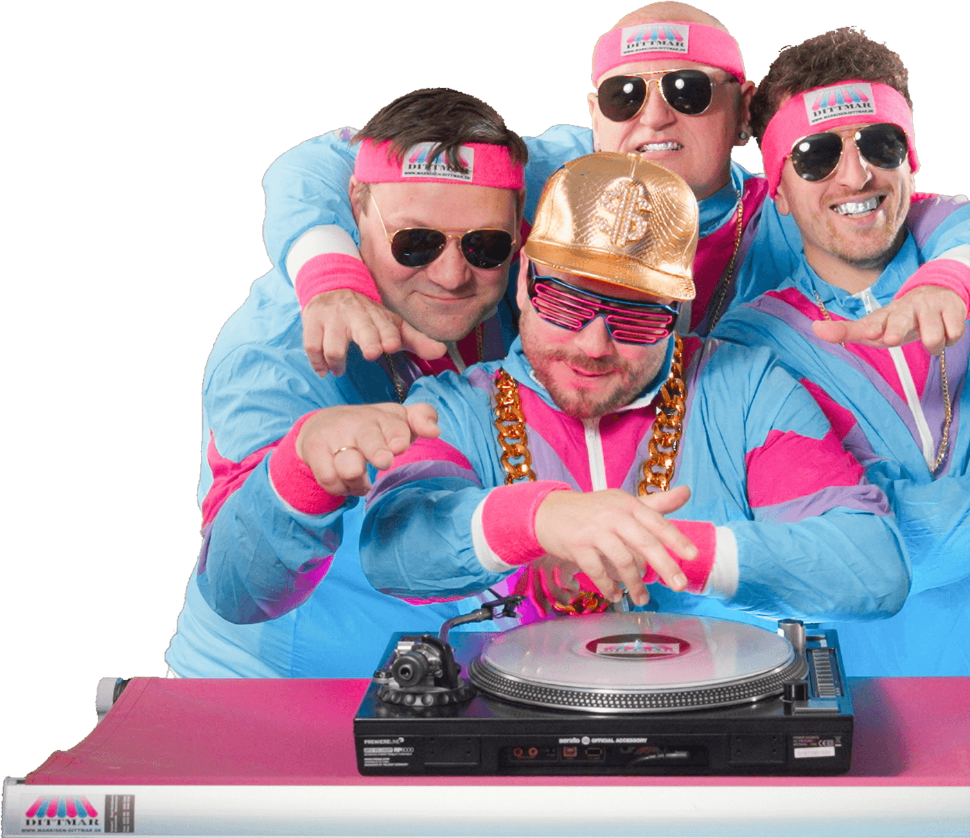 Vier Männer in farbenfrohen 80er-Jahre-Outfits posieren als DJs um einen Plattenspieler herum, lächeln und tragen lustige Accessoires.